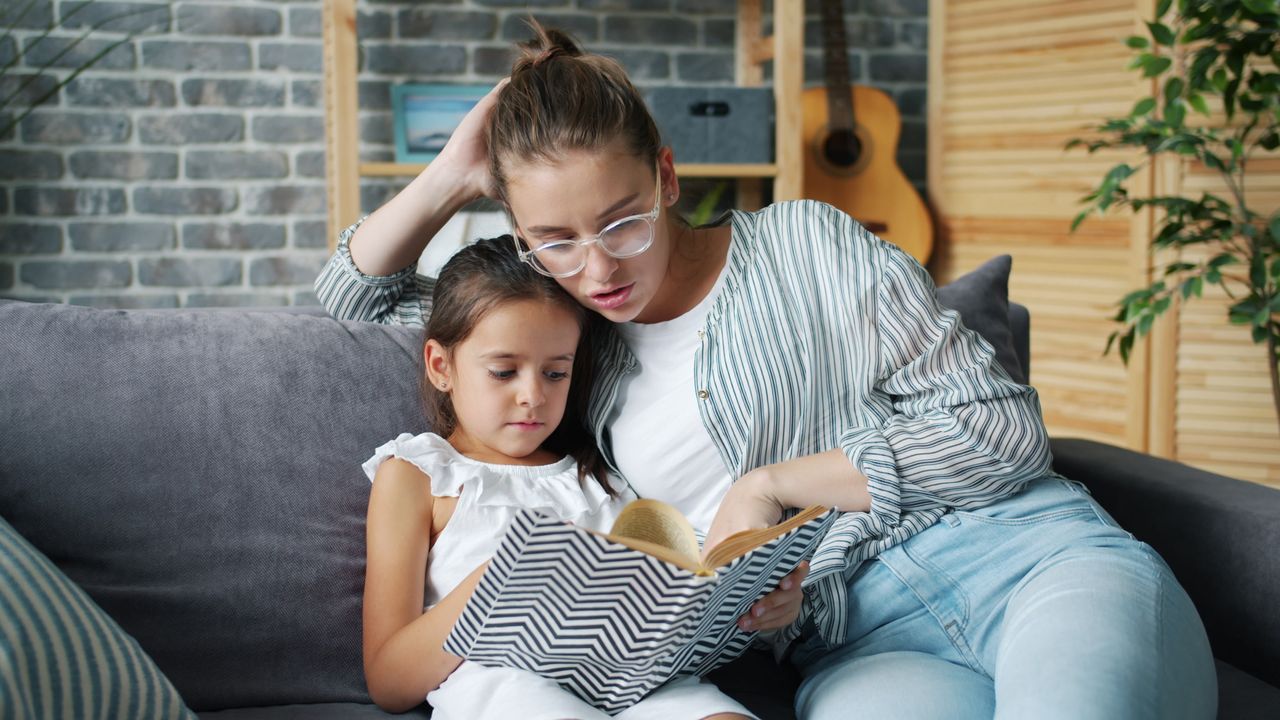 A mother and daughter bonding over a book on the sofa in a cozy living room.