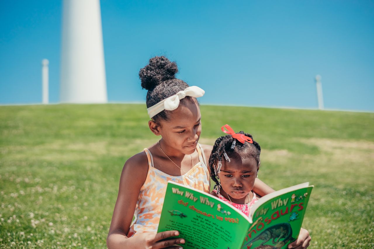 Two young sisters enjoying a book together on a sunny day in the park, emphasizing childhood joy and learning.